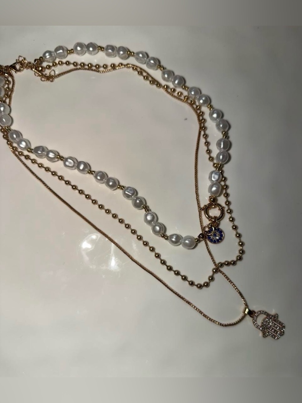 Multi-layered pearl necklace with gold chains and Hamsa hand charms evil eye